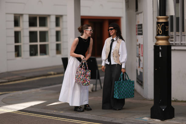 Fashion Show Guest was seen wearing black shoes, a colorful bag white wide shorts, a black top and white shades next to a person wearing wide and...