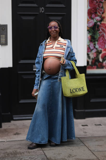 Fashion week guest is seen wearing a crop top with red and orange stripes and collar by Miu Miu with a blue denim jacket, a long denim skirt, black...