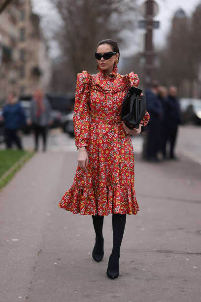 Fashion Week guest is seen wearing Balenciaga Outfit including black heels, black tights, a black bag, black shades and a red dress with white and...