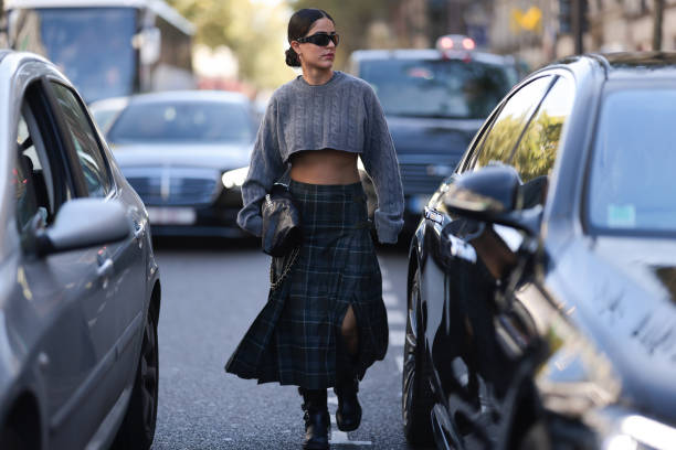Fashion Week guest is seen wearing black chades, yellow gold earrings, a grey cropped Miu Miu shirt, a black Chanel bag and a green checked long...
