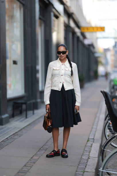 Fashion Week guest is seen wearing large black sunglasses, several silver hoop earrings, a buttoned cream-white structured jacket with red decorative...