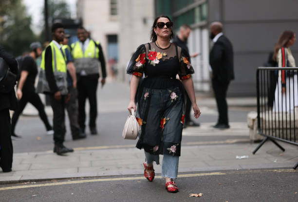 Fashion Week Guest was seen wearing red leather shoes, a denim jeans, abbeige bag, dark shades, a black top under a black transparent dress with...