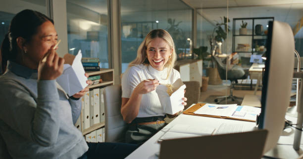 fast food, delivery and business women at night in office with computer, project and happy, working and deadline. working late, noodles and female friends laughing on work break for dinner or meal - junk food stock pictures, 