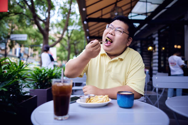 fat chinese man eating french fries - junk food stock pictures, royalty-free photos & images