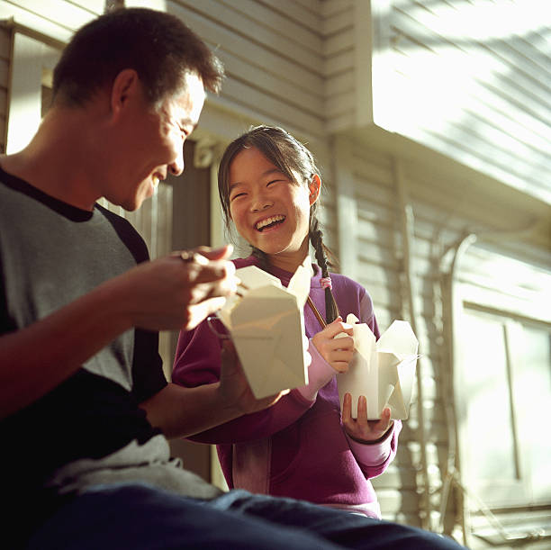 father and daughter (12-14) eating chinese food, laughing - junk food stock pictures, royalty-free photos & images
