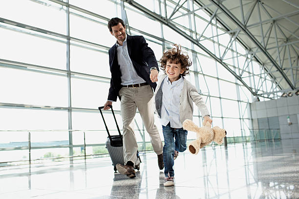 father and son (5-6) running across airport lobby - travel stock pictures, royalty-free photos & images