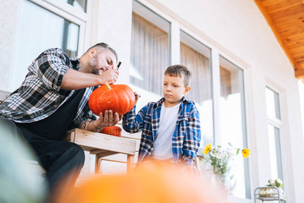 father and son drawing jack on pumpkin for halloween in the back yard of house - garden decoration stock pictures, royalty-free photos & images
