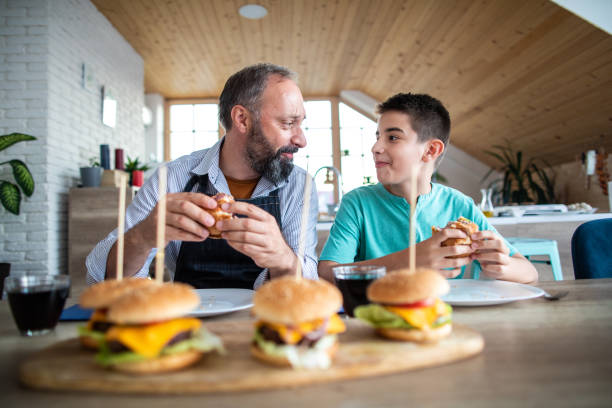 father and son eating slider - burgers at home - junk food stock pictures, royalty-free photos & images