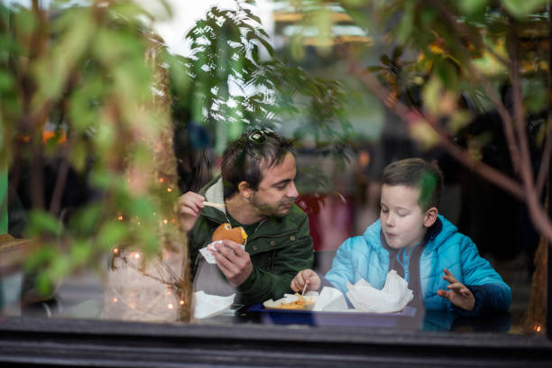 father and son having discussion and lunch at fast food restaurant - junk food stock pictures, royalty-free photos & images