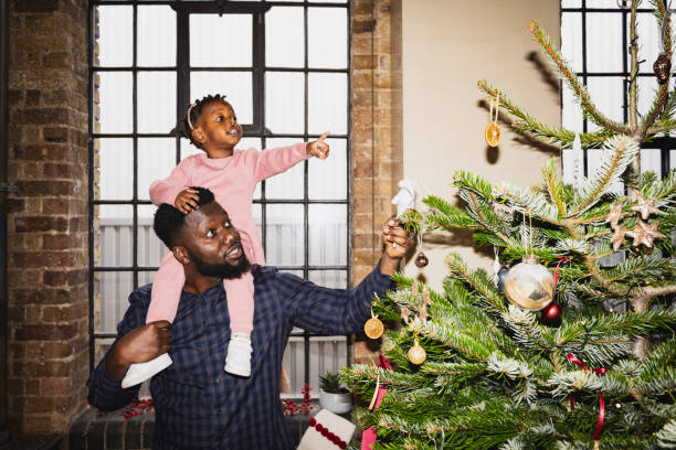 father and young daughter admiring christmas tree decorations - home decoration stockfoto's en -beelden