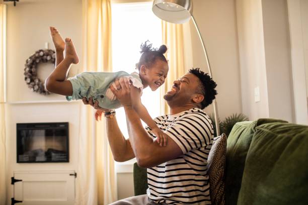 father lifting toddler daughter in the air - home decoration photos et images de collection