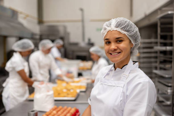 female baker working at an industrial bakery and smiling - food stock pictures, royalty-free photos & images