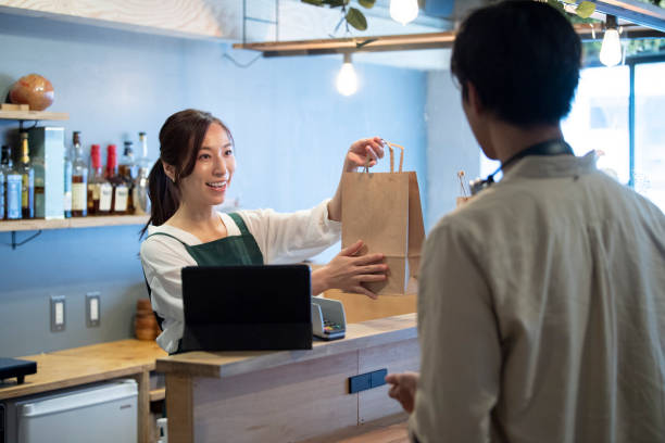 female cafe staff giving a paper bag of take-out food to a male customer - junk food stock pictures, royalty-free photos & images