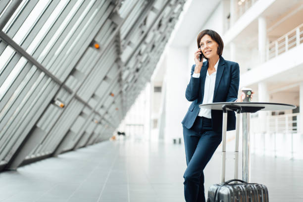 female entrepreneur with coffee cup talking on smart phone in corridor - junk food stock pictures, royalty-free photos & images