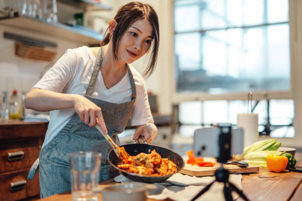 female food blogger cooking pasta and recording video on smart phone - food stockfoto's en -beelden