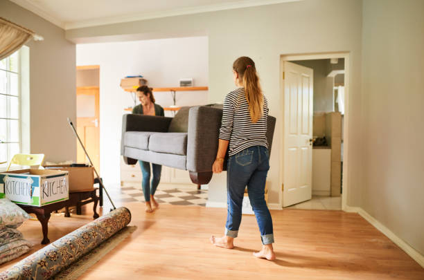 female friends carrying a sofa out of a house on moving day - home decoration stockfoto's en -beelden
