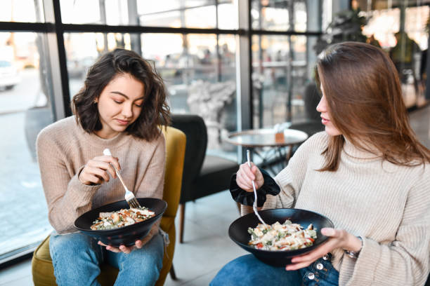 female friends enjoying healthy salad meal in restaurant - junk food stock pictures, royalty-free photos & images