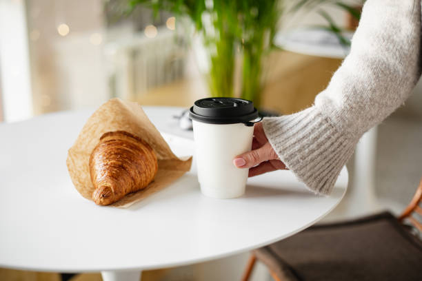 female hand holding a disposable glass with coffee and fresh croissant. concept of delivery food - junk food stock pictures, royalty-free photos & images