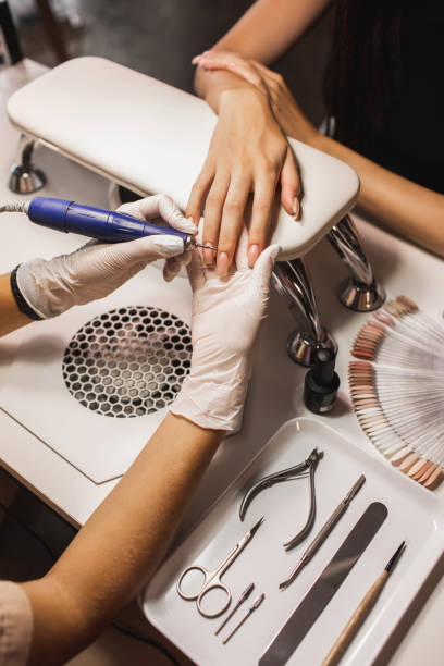 female hands while manicurist filing and polishing fingernails with professional device, making hardware manicure using electric machine in beauty studio. - nails art stock pictures, royalty-free photos & images