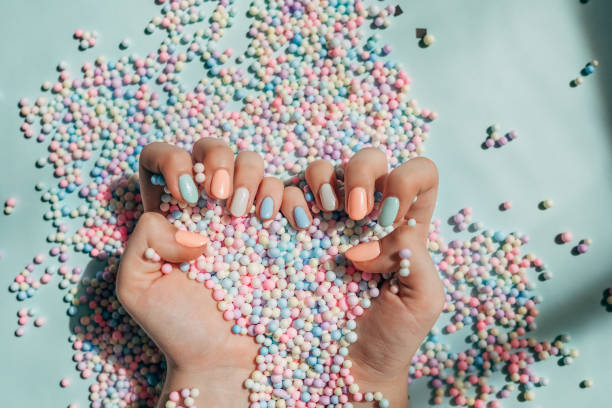 female hands with trendy colorful french manicure are lying on a pastel background, divided into light green and light pink part with many round paper confetti. - nails art stock pictures, royalty-free photos & images