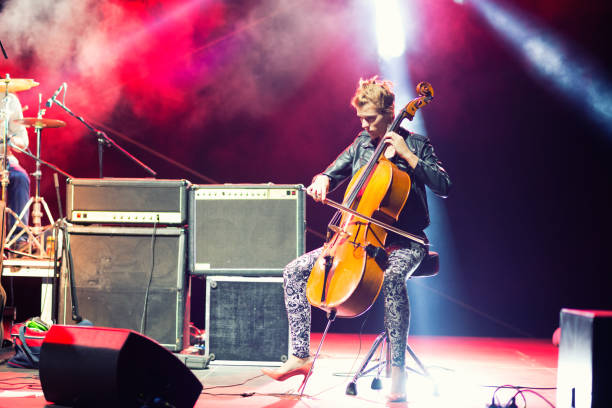 female musician playing cello on stage under spotlights - concert stock pictures, royalty-free photos & images