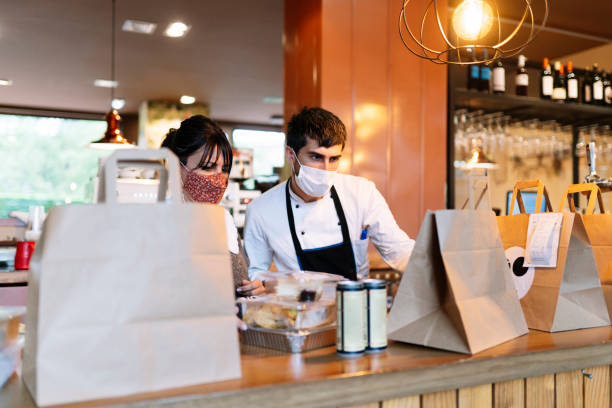 female owner and male chef checking take out food orders on bar counter during pandemic - junk food stock pictures, royalty-free photos & images
