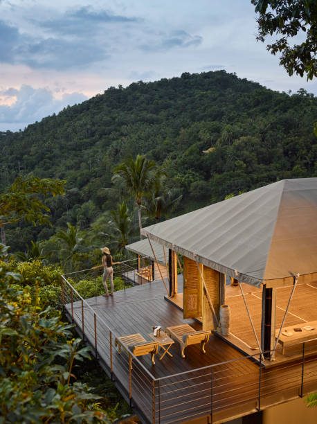 female tourist admiring sea view while standing on decking of tented villa, at eco friendly luxury glamping resort, at dawn - travel stock pictures, royalty-free photos & images