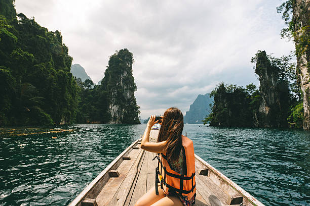 female tourist exploring lush jungle lake surrounded by limestone cliffs, khao sok national park, thailand - travel stock pictures, royalty-free photos & images