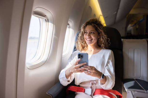female traveler using her cell phone in an airplane - travel stock pictures, royalty-free photos & images