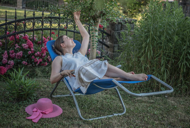 femme assise dans une chaise longue, se relaxant dans le jardin l’après-midi d’été - garden decoration photos et images de collection