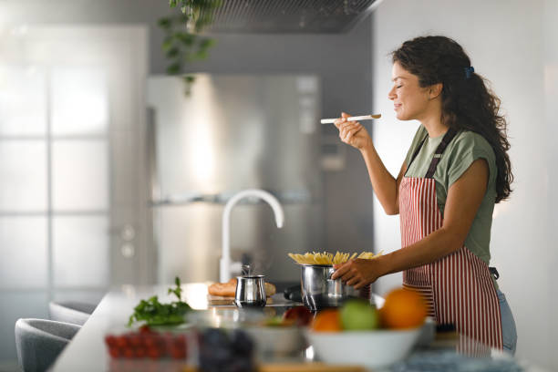 femme souriante appréciant tout en cuisinant des spaghettis pour le déjeuner. - food photos et images de collection
