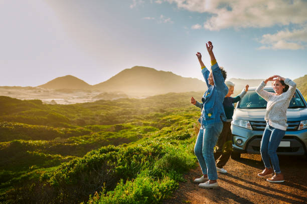femmes d’âge mûr applaudissant près de leur voiture garée près d’une côte pittoresque lors d’un voyage en voiture - travel photos et images de collection