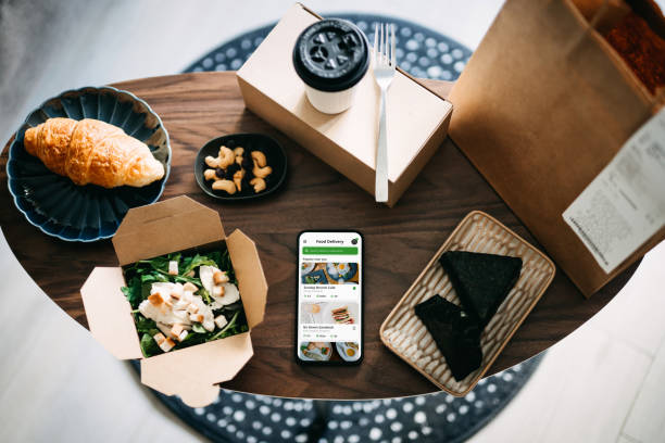 flat lay of takeaway food ordering mobile app on smartphone, with assorted takeaway dishes, healthy grilled chicken vegetable salad, croissant, japanese style rice ball / onigiri and a cup of coffee freshly served on coffee t