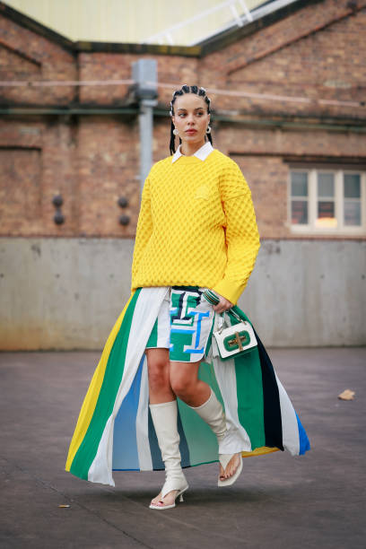 Fleur Egan wearing buttons on her hair, yellow jumper, green and blue mixed colour maxi split skirt, white boots and green and white bag during...