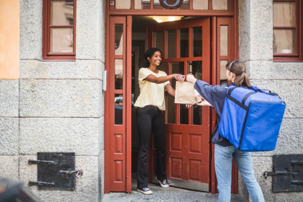 food delivery woman delivering package to customer standing at doorway in city - food stock pictures, royalty-free photos & images