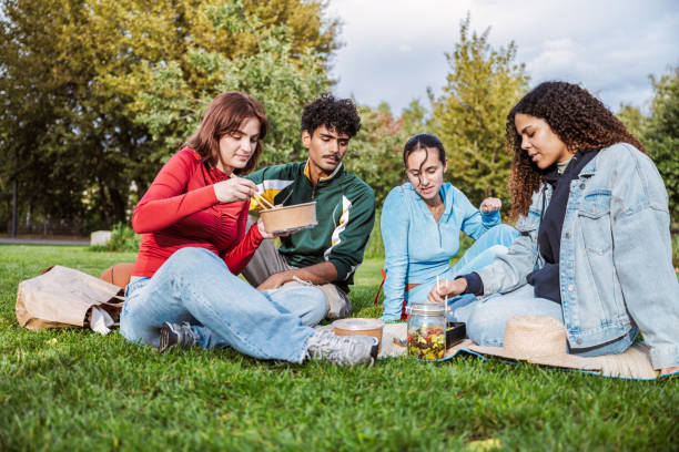 four young people having picnic in the park - junk food stock pictures, royalty-free photos & images