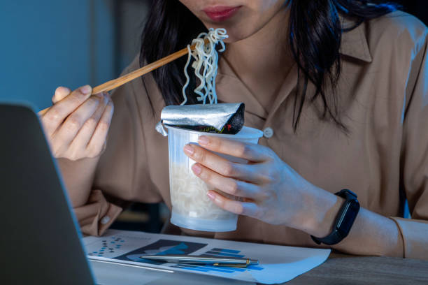 freelance women eating instant noodles while working on laptop in living room at home at night. - junk food stock pictures, royalty-free photos & images