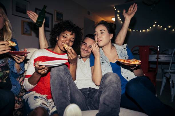 friends eating pizza on sofa during party at home - junk food stock pictures, royalty-free photos & images