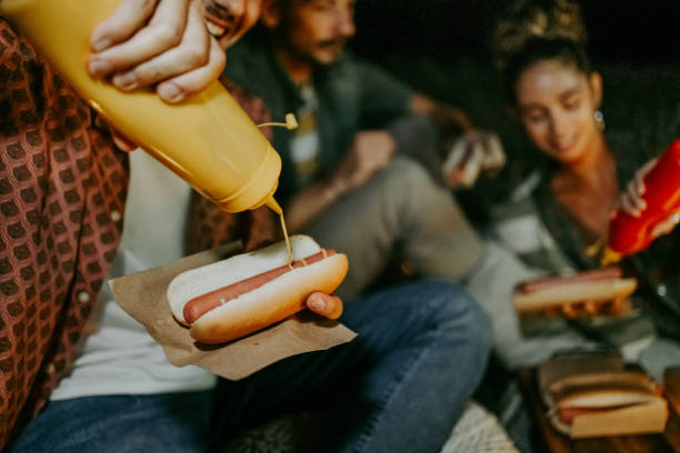 friends enjoying hot dogs while camping outdoors - junk food stock pictures, royalty-free photos & images