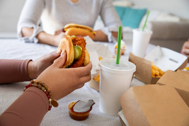 friends smile and laugh while enjoying fast food they had delivered to their home. they're eating burgers and fries - junk food stock pictures, royalty-free photos & images