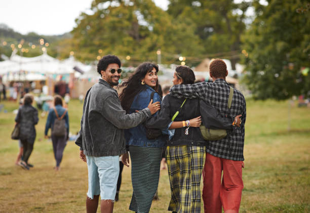 friends walking side by side with arms around at park - concert stock pictures, royalty-free photos & images