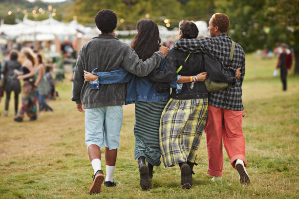 friends with arms around walking side by side at park - concert stock pictures, royalty-free photos & images