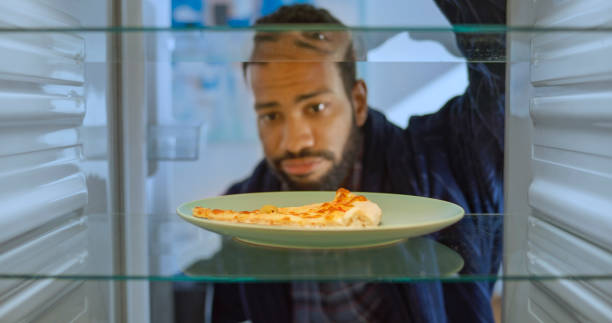 frowning man looking slice of pizza - junk food stock pictures, royalty-free photos & images