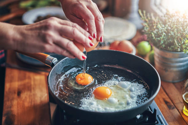 frying egg in a cooking pan in domestic kitchen - food stock pictures, royalty-free photos & images