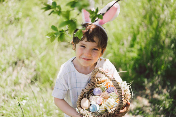 funny boy with eggs basket and bunny ears on easter egg hunt in sunny spring garden - garden decoration stock pictures, royalty-free photos & images