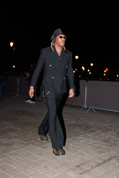 Future wears a scarf over the head, sunglasses, a black double breasted blazer jacket , flared pants, studded black leather shoes, before the Louis...