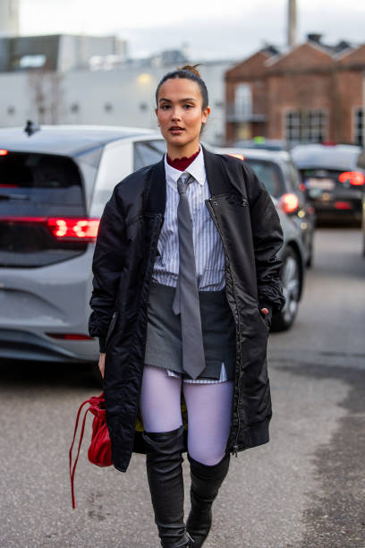 Gabriela Sevillano Fernández wears black bomber coat, red bag, over knees boots, grey tie, button shirt outside Mfpen during the Copenhagen Fashion...
