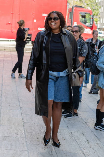 Gabriella Karefa-Johnson is seen wearing a brown leather coat, blue top, blue denim shorts, black sunglasses, black shoes and carrying a grey bag...