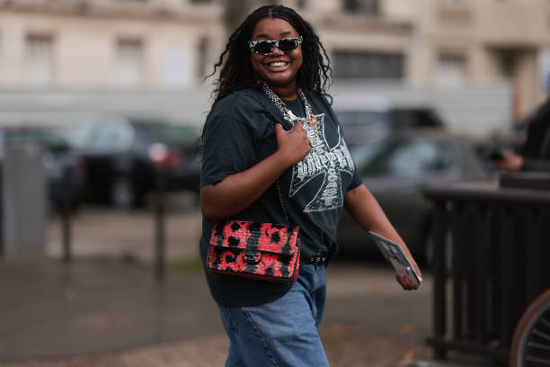 Gabriella Karefa Johnson is seen outside Chanel show wearing black and white Balenciaga sunnies, silver necklaces, grey vintage band t-shirt, long...