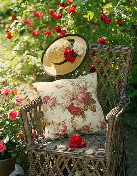 garden wicker chair with cushion and straw hat surrounded by roses - garden decoration stockfoto's en -beelden